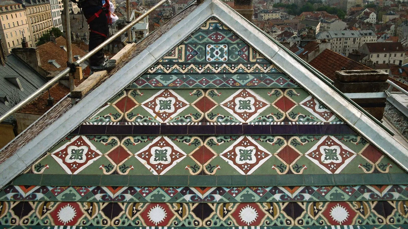 Couvreur au travail sur un toit dijonnais en tuiles vernissées polychromes, toits du centre ancien en arrière-plan